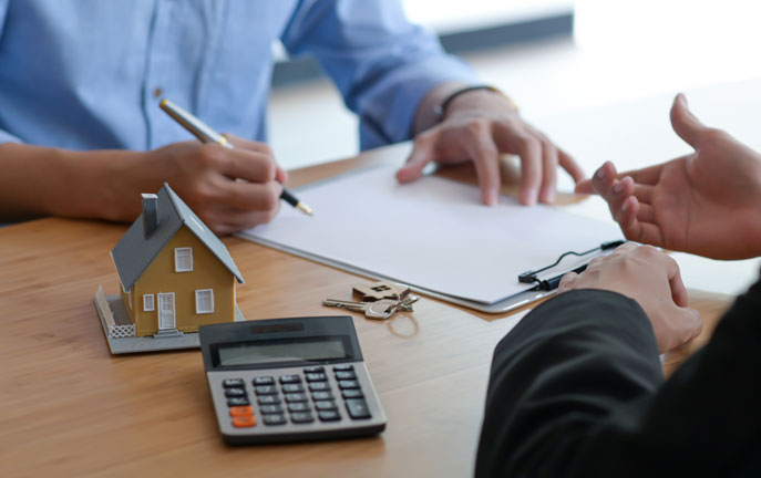 Immobilienverkauf mit Rentenzahlung wird berechnet. Mann unterschreibt Vertrag mit Haus, Schlüssel und Rechner auf dem Tisch.